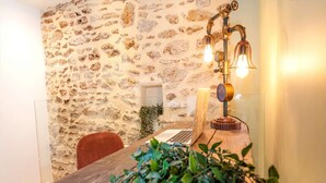A rustic stone wall, a wooden table with a laptop, a red chair, and a vintage lamp. - Géranimus 199 : Art of Paris (Paris)