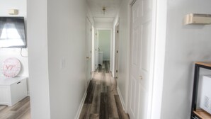 Un corridoio con pavimento in legno, pareti bianche e una porta in fondo.