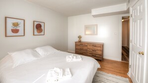 Una camera da letto con un letto, una cassettiera in legno e una porta che conduce a un'altra stanza.