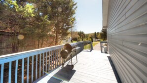 Una terrazza con barbecue, ringhiera e vista su alberi e una casa.