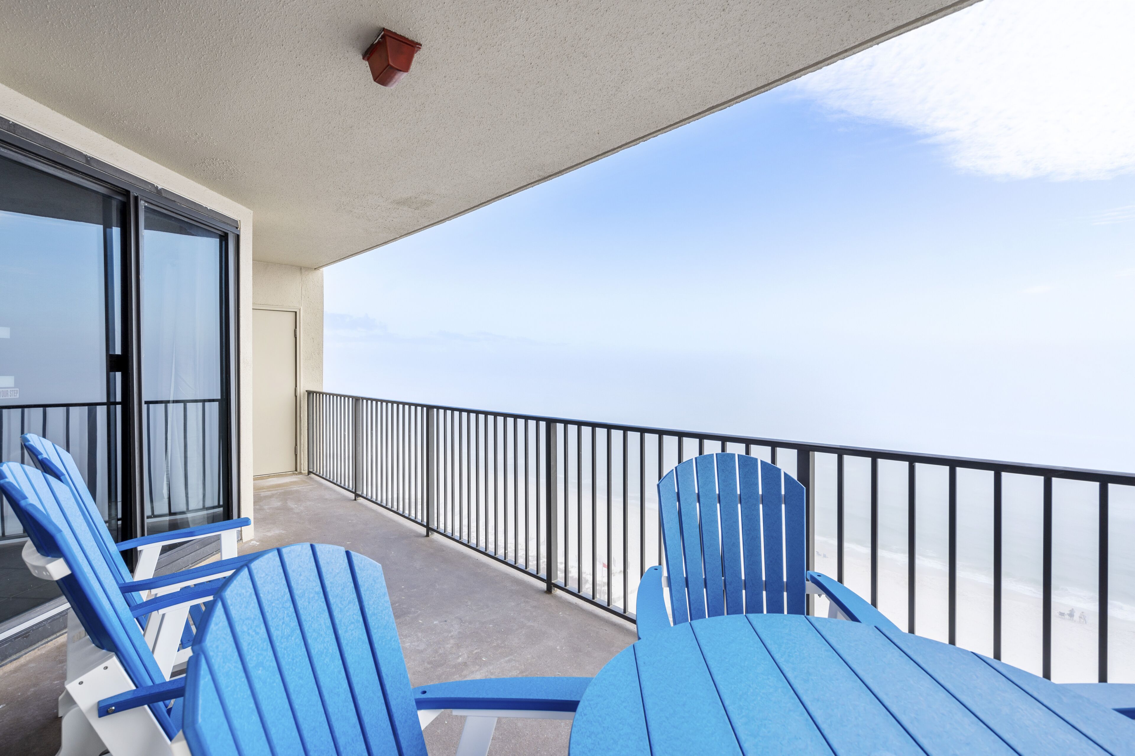 A balcony with blue Adirondack chairs, a glass door, and a view of the ocean.