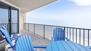 A balcony with blue Adirondack chairs, a glass door, and a view of the ocean.