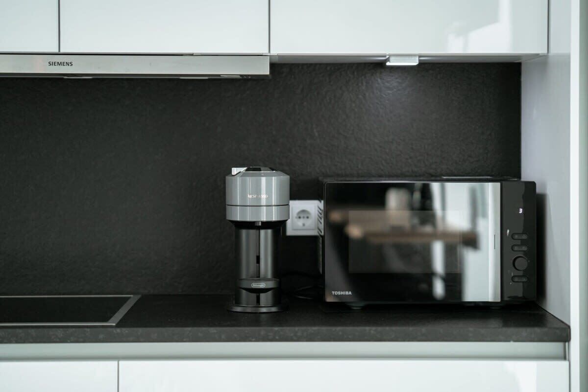 Eine Küche mit einer Siemens-Kaffeemaschine und einer Toshiba-Mikrowelle auf einer schwarzen Arbeitsplatte.