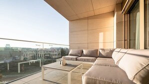 En moderne balkon med en beige hjørnesofa, et lille bord og gelænder af glas.