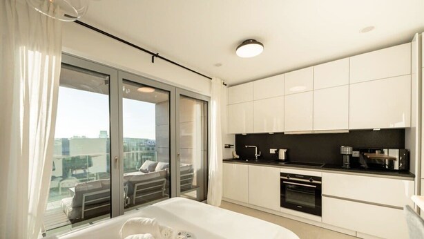 Et moderne hotelværelse med en stor seng, et tekøkken og en skydedør til en balkon.
