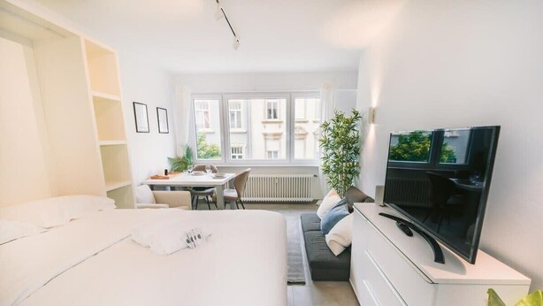 A modern hotel room with a large bed, a desk, a TV, and a window with a city view.