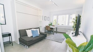 A modern living room with a grey sofa, a dining table with chairs, a white radiator, and a large green plant.