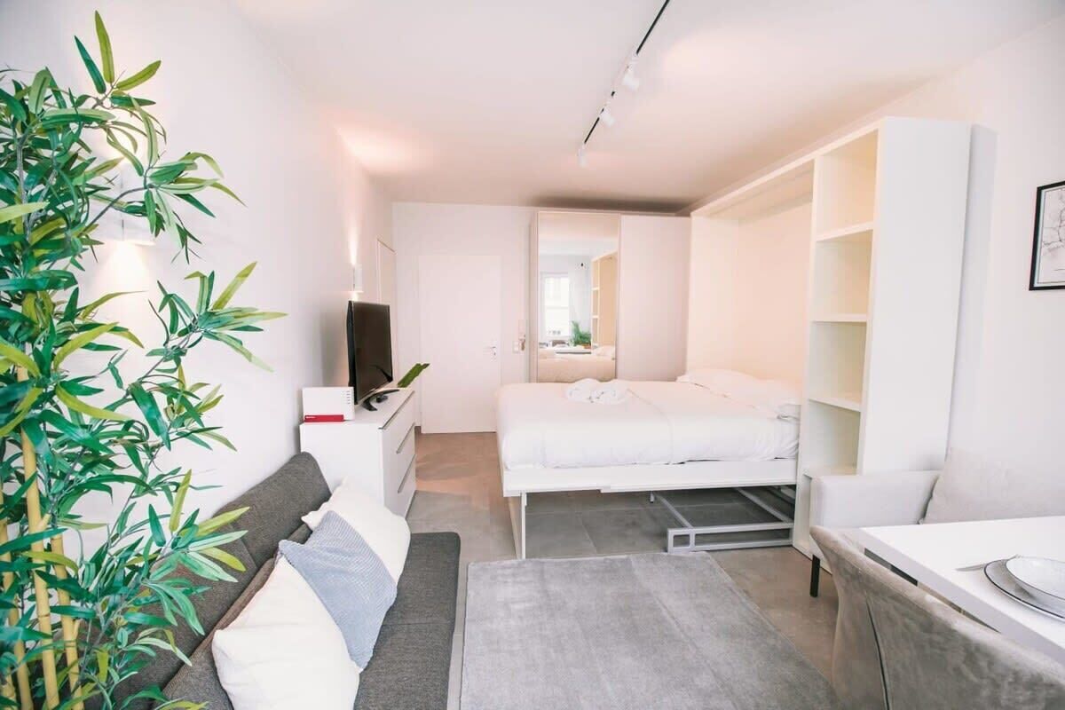 A modern, compact hotel room with a bed, bedside tables, a desk, and a large mirror.