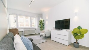 A modern living room with a grey sofa, white armchair, and a flat-screen TV on a white cabinet.