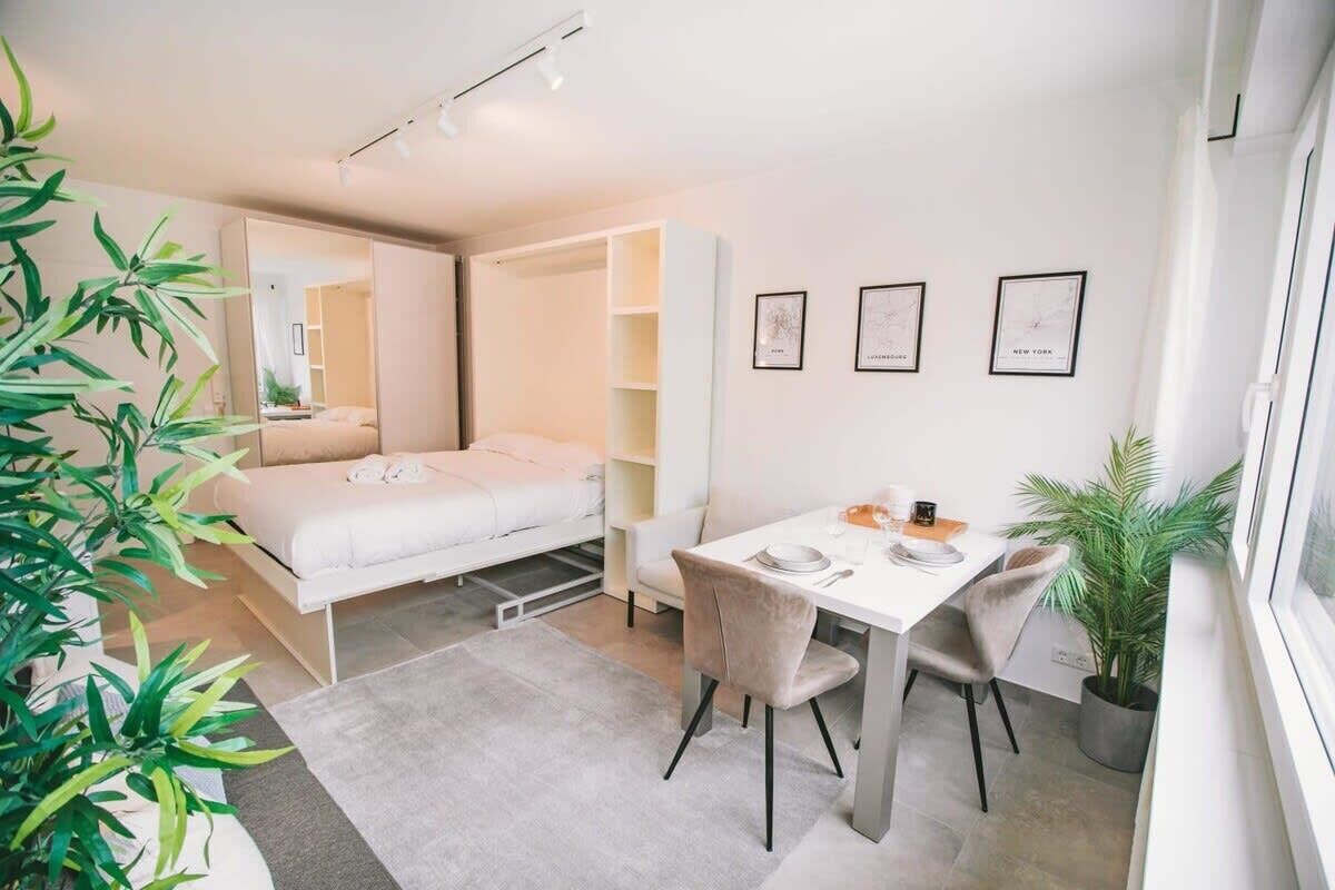 Un dormitorio moderno y funcional con cama, escritorio y silla. Hay cuadros enmarcados en la pared y una planta en maceta cerca de la ventana.