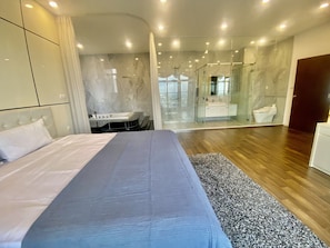Une chambre moderne avec un grand lit, une salle de bain dotée d’une douche en verre et un plancher en bois.