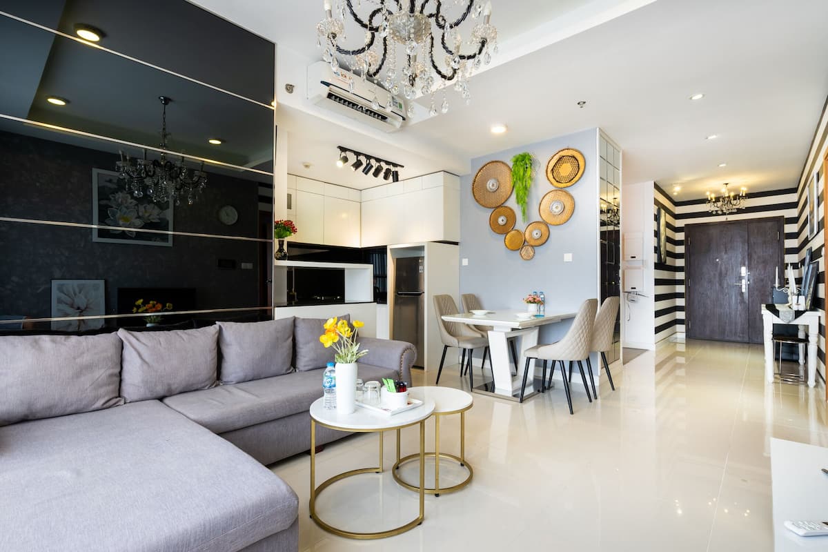 A modern living room with a grey sofa, a dining area with a white table and chairs, and a kitchen in the background.
