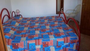 Une petite pièce simple, avec un lit, une chaise, une table de chevet et un miroir au mur.
