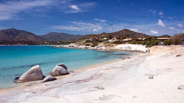 Une plage avec une eau turquoise et limpide, du sable blanc et de gros rochers au premier plan.