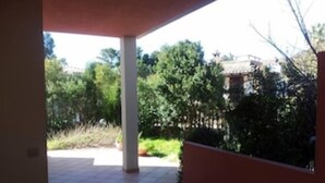 Un patio couvert doté d’un sol carrelé et offrant une vue sur un jardin agrémenté d’arbres et d’arbustes.