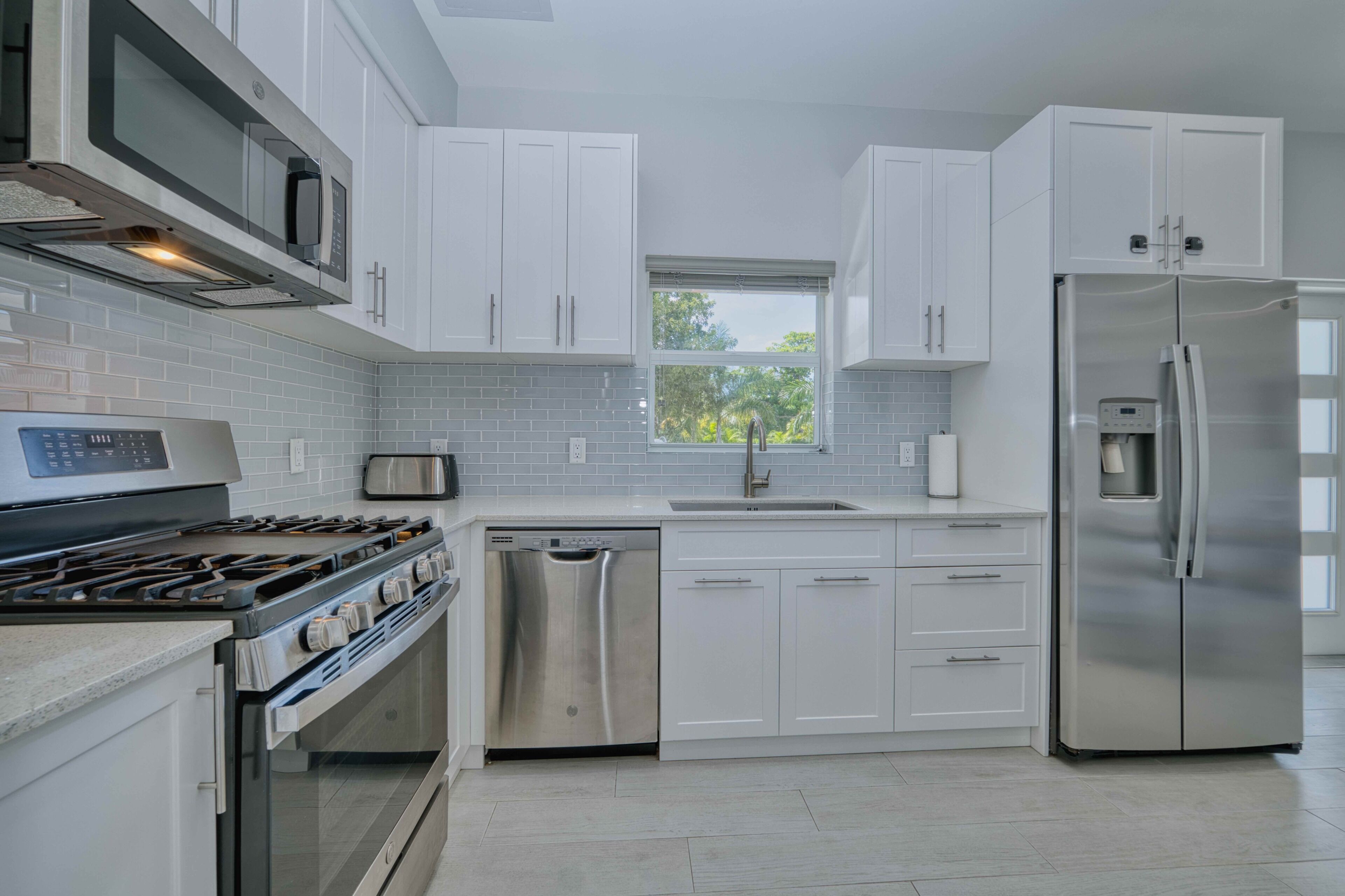 A modern kitchen with white cabinets, stainless steel appliances, and a window providing natural light.