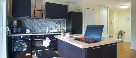 A compact kitchen with modern appliances, a washing machine, and a laptop on the counter.