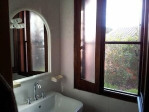 A bathroom with a white bathtub, a mirror with an arched top, and a window with a view of greenery outside.