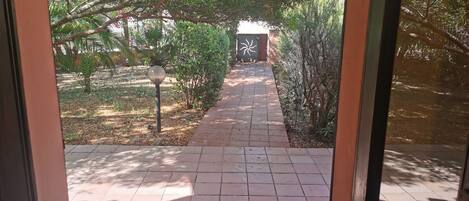 A pathway leading to a building with a distinctive door design, surrounded by greenery and a tiled walkway.