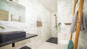 A modern bathroom with a marble backsplash, a black sink, a white toilet, and a shower area.