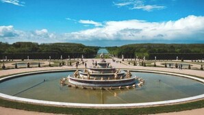A large circular fountain with statues in the center, surrounded by a well-maintained garden and pathways.
