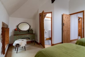 A bedroom with a green bed, a wooden dresser with a mirror, a small stool, and a door leading to a bathroom.
