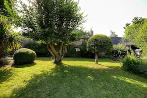 A well-maintained garden with various trees and shrubs, a neatly trimmed lawn, and a stone building in the background.
