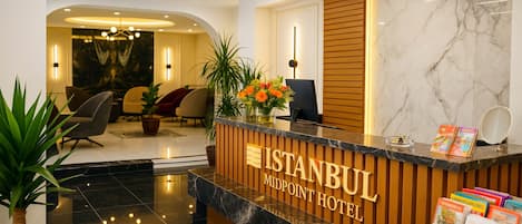 Mostrador de recepción en el Hotel Midpoint de Estambul, con piso de mármol, plantas en macetas y vista al área del vestíbulo.
