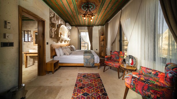 A room with a bed, a colorful chair, a rug, and a ceiling with a unique design.
