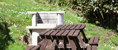Une table de pique-nique se trouve dans un espace herbeux, avec un banc en pierre en arrière-plan.