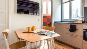 Cozinha compacta com área de refeições, apresentando uma mesa de madeira, cadeiras, forno embutido e uma janela com vista.