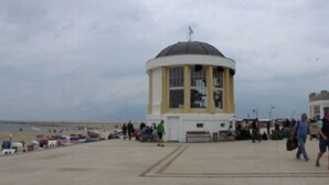 Ein Küstengebäude mit Kuppel, einem gepflasterten Weg und Personen im Hintergrund.