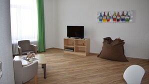 Ein modernes Wohnzimmer mit einem Flachbildfernseher auf einem Holzständer, einem Esstisch mit Stühlen, einer Couch und einem Sitzsack.