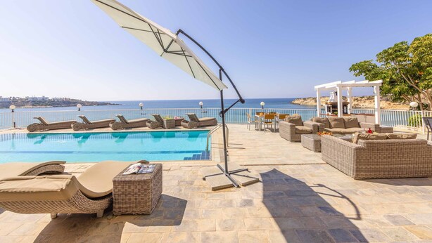 Un área junto a la piscina con sillones, un espacio de descanso cubierto y vista al mar.