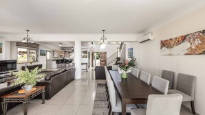 Amplia sala de estar con una larga mesa de comedor, asientos cómodos, zona de cocina y una escalera que conduce a un piso superior.