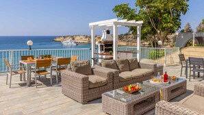 Una terraza con mobiliario de mimbre, una parrilla y vistas al mar.