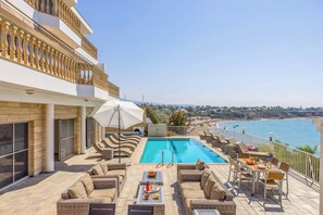 A rooftop pool with lounge chairs and a table, overlooking a coastal area.