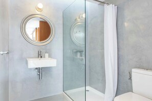 A modern bathroom with a glass-enclosed shower, a round mirror, and a white sink. - Villa Ullastres Ses Alzines (Sant Lluís)