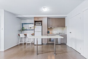 Una cocina funcional con una mesa blanca, dos taburetes de bar, un microondas, un refrigerador y armarios de madera.