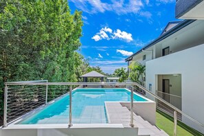A swimming pool with a metal railing, surrounded by greenery and a clear sky. - Casa D' Amore' (Airlie Beach)