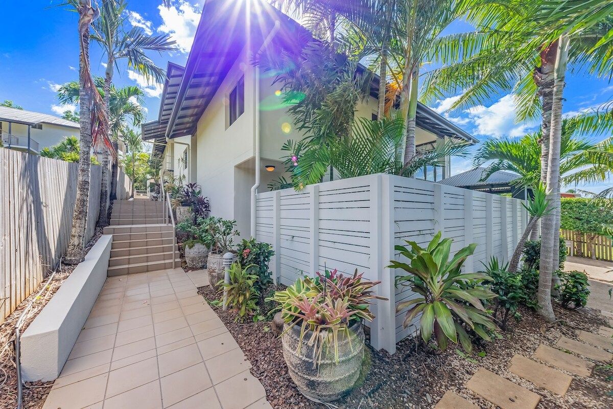 A residential property with a paved driveway, a wooden fence, and various potted plants.