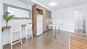 Cozinha moderna com eletrodomésticos brancos, bancada de madeira e dois banquetes brancos.