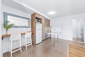 A modern kitchen with white appliances, a wooden countertop, and two white bar stools. - Casa D' Amore' (Airlie Beach)