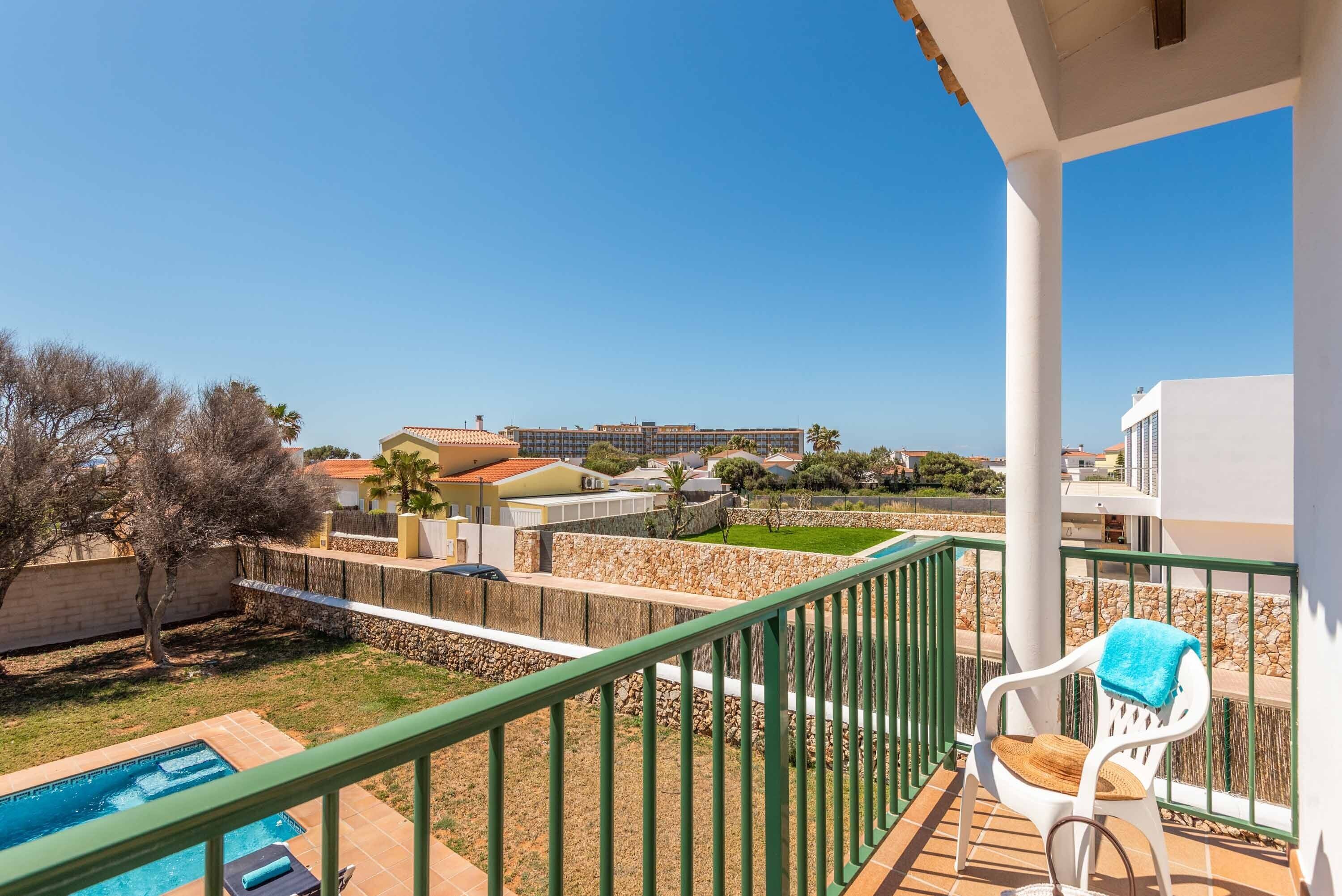 A balcony with a view of a swimming pool, a chair with a towel, and a stone wall.