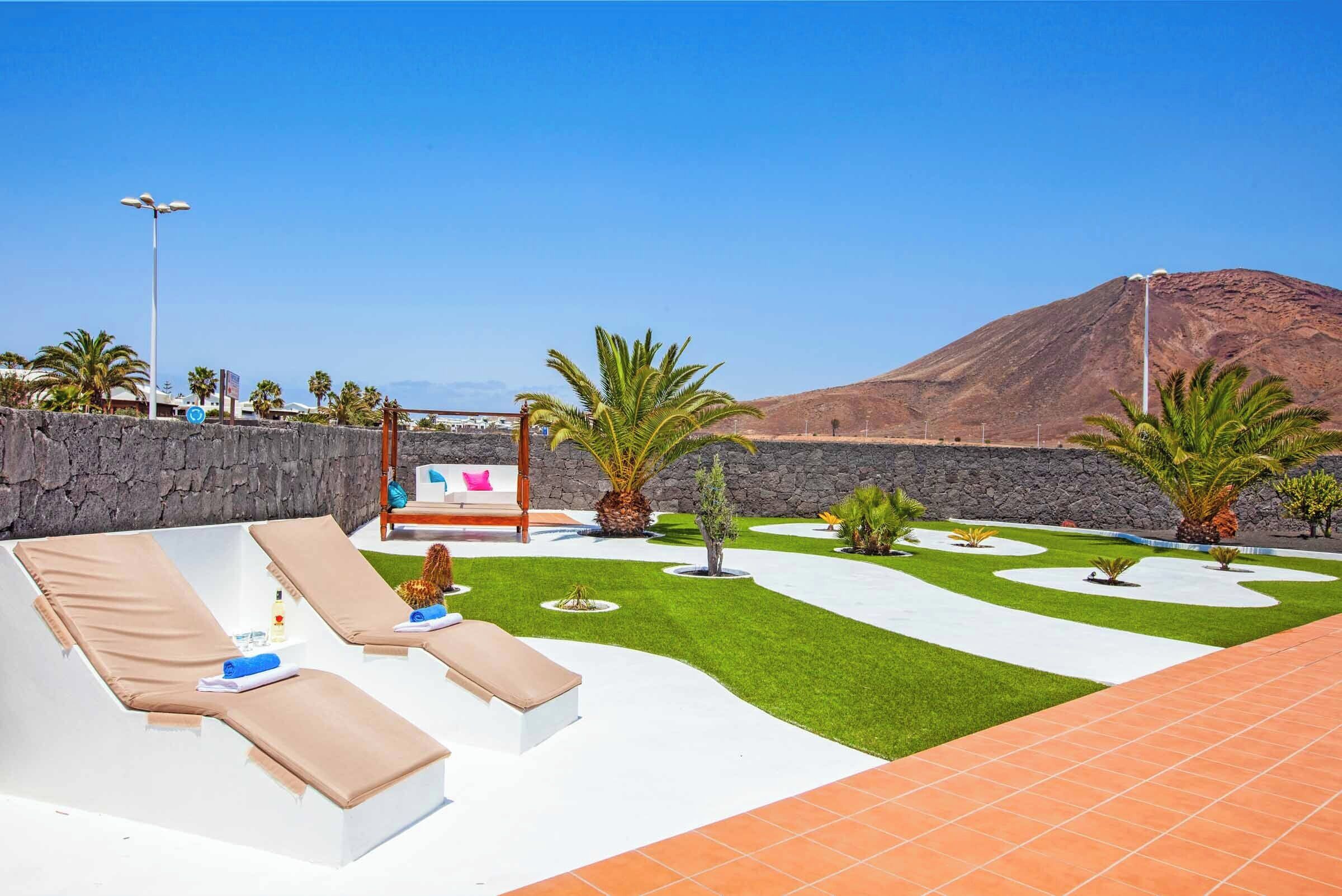 Un área de lounge en la azotea con sillones de sol, un muro de piedra y vistas a la montaña.
