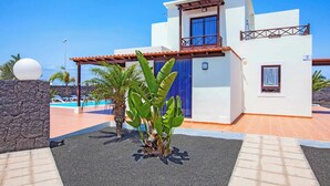 Une maison moderne à deux étages, dotée d’un balcon, d’une piscine et de plantes tropicales.