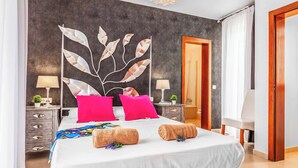 Une chambre moderne avec un grand lit, deux tables de chevet, une décoration murale représentant des feuilles et une porte en bois.