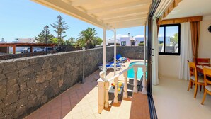 Un balcón techado con piscina, pared de piedra y mobiliario exterior.