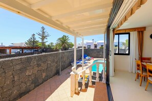 Ein überdachter Balkon mit Pool, Steinmauer und Gartenmöbeln.