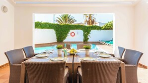 Comedor con vista a la piscina, mobiliario de mimbre y una mesa lista para cuatro.